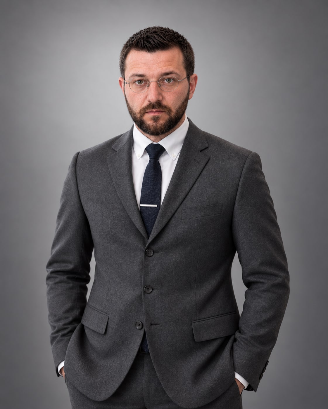 Alexander Körbel im dunklen Dreiknopfsakko mit Krawatte vor grauem Hintergrund.